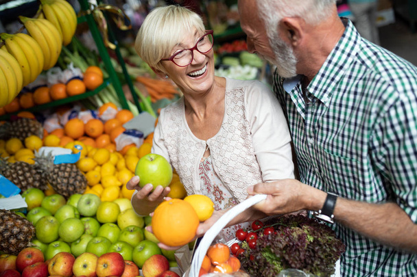 Smiling senior couple holding basket with vegetables at the grocery shop - Photo, Image