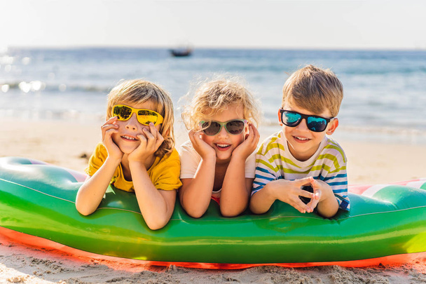 Three blond kids in sunglasses are lying on the beach - Foto, afbeelding