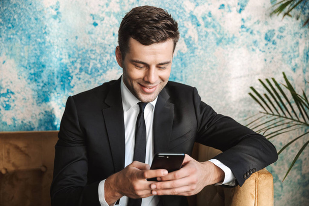 Happy young businessman sitting in cafe using mobile phone. - Foto, Bild