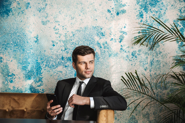 Young businessman sitting in cafe using mobile phone. - Photo, image