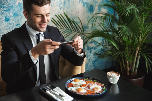 Businessman sitting in cafe take a photo of food by mobile phone. - Foto, imagen