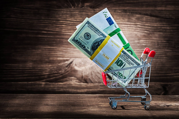 bundles of dollars and euro in shopping cart on vintage wood - Photo, image