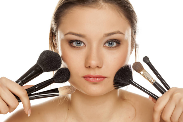 Chica joven posando con pinceles de maquillaje sobre un fondo blanco
 - Foto, Imagen