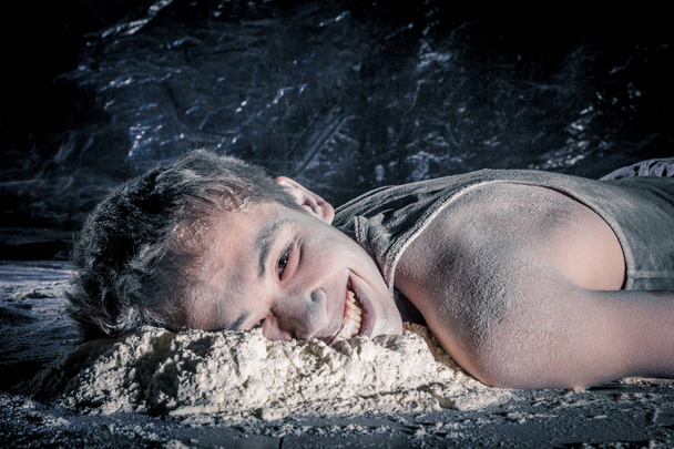 happy korean guy lying on the floor with a soiled face in white powder on black background. concept of absolute joy, indifference and human carelessness. - Photo, Image