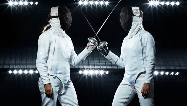 Young fencer athlete wearing mask and white fencing costume. holding the sword on black background with lights. - Fotó, kép