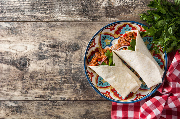 Typische mexikanische Burrito-Wrap mit Rindfleisch, Frijoles und Gemüse auf einem Holztisch. Ansicht von oben. Kopierraum - Foto, Bild