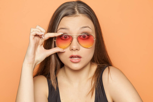 junges Mädchen mit orangefarbener Sonnenbrille auf orangefarbenem Hintergrund - Foto, Bild