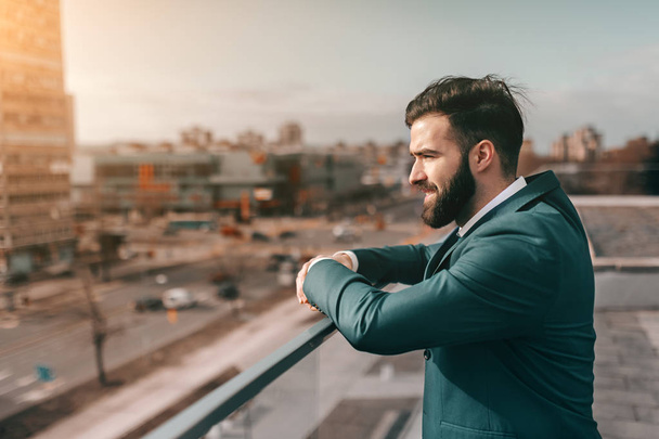 Profile of bearded businessman leaning on the fence and looking at view while standing on rooftop. - 写真・画像