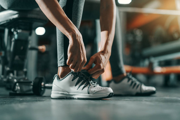 Close up of slim Caucasian woman tying shoelace in gym at night. Be stronger than your excuses. - 写真・画像
