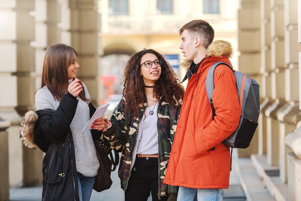 Tres sonrientes amigos multiculturales felices de pie frente a la escuela y charlando
. - Foto, Imagen