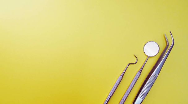 Профессиональные инструменты дантиста в стоматологической клинике. Зеркало стоматолога, щипцы изогнутые, исследователь изогнутый, исследователь зубов угловатый и исследователь изогнутый с чипом на желтом фоне
 - Фото, изображение