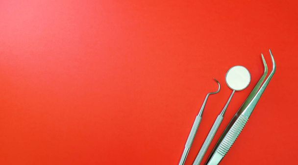 Professional dentist instruments in dental office. Dentist mirror, forceps curved, explorer curved, dental explorer angular and explorer curved with chip at red background - Photo, Image