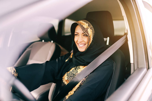 Beautiful muslim woman with toothy smile driving car. - Zdjęcie, obraz
