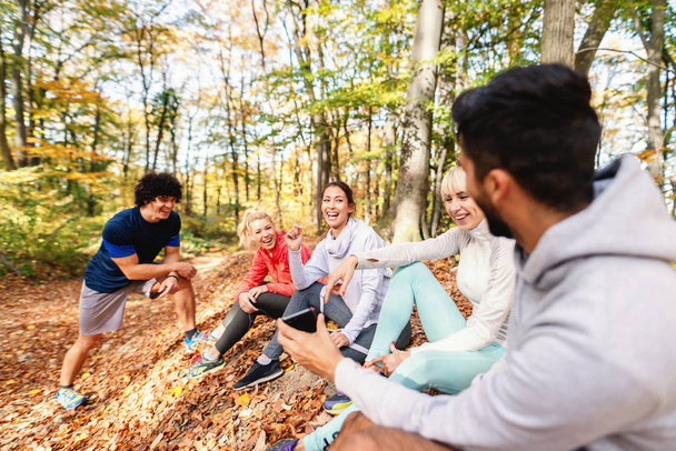 Pequeño grupo de deportistas sentados en el bosque en otoño y descansando de correr y hacer ejercicio. Fitness en el concepto de naturaleza
. - Foto, imagen