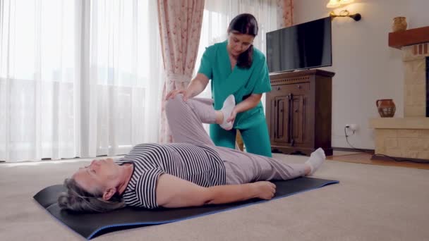 Mladý terapeut cvičení se starší pacientka v pečovatelském domě. Zdravotní sestra dává masáž nohou, starší žena v domov důchodců. Slow motion 4k ruční hnutí - Záběry, video