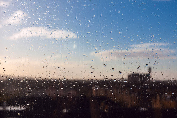 Blurred urban background with blue cloudy sky behind wet window - Photo, Image