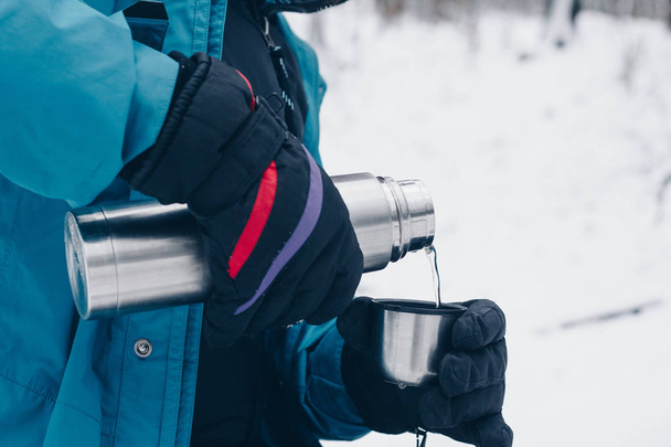 Wanderer gießt Tee aus der Thermoskanne im Winterwald - Foto, Bild