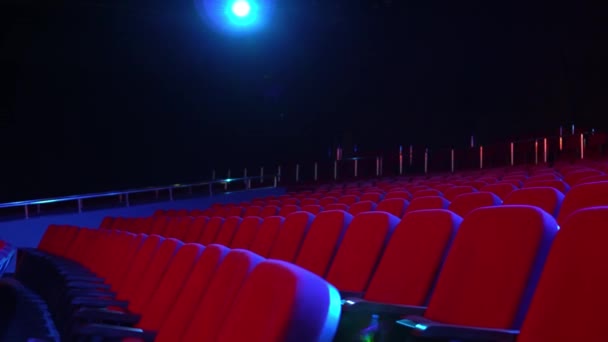 Lege rijen van zitplaatsen in bioscoop zaal. Lege bioscoop met rode zetels in verduisterde kamer met projector licht op de achtergrond - Video