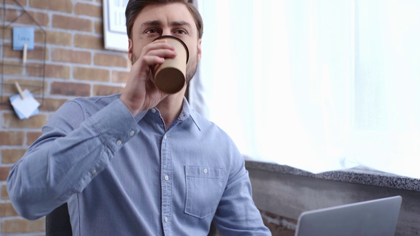 Συμπυκνωμένο επιχειρηματία σε μπλε πουκάμισο χρησιμοποιώντας φορητό υπολογιστή και να πίνει καφέ στο χώρο εργασίας - Πλάνα, βίντεο