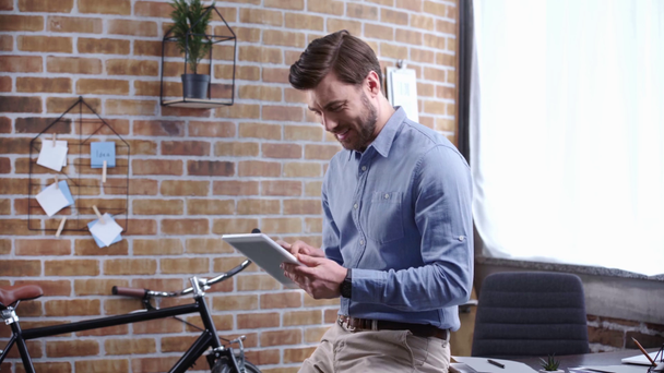 Konzentrierter Geschäftsmann im blauen Hemd sitzt am Tisch und benutzt am Arbeitsplatz lächelnd ein digitales Tablet - Filmmaterial, Video