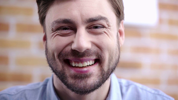 Handsome man with beard starting to laughing and blinking while looking at camera - Footage, Video
