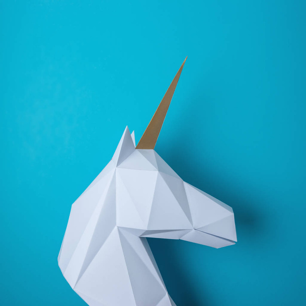 White 3d papercraft model of unicorn head on blue background. Minimal art concept. - 写真・画像