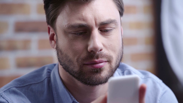 Handsome concentrated brunette businessman in blue shirt scrolling and typing on smartphone - Metraje, vídeo