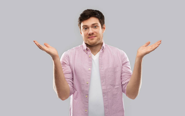 young man shrugging over grey background - Photo, Image