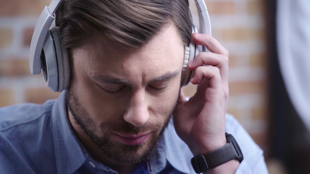 Νεαρός άνδρας με το ρολόι κυματίζοντας κεφάλι ενώ ακούτε μουσική και συγκινητικό λευκά ακουστικά - Πλάνα, βίντεο