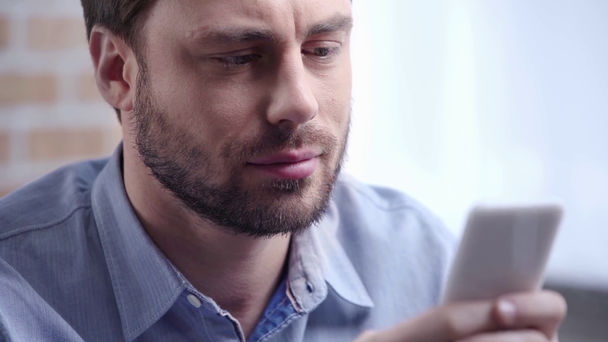 Hombre de negocios guapo en camisa azul con barba parpadeando mientras escribe en el teléfono inteligente
 - Metraje, vídeo