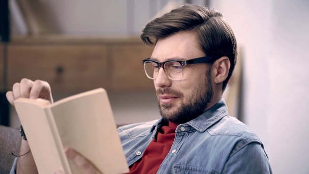 Zúčastněné mladý muž v brýlích, čtení knihy, kroutil hlavou udiveně a otáčení stránek - Záběry, video