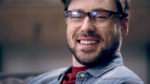 Handsome young man in glasses turning at camera and starting to laugh at home - Footage, Video