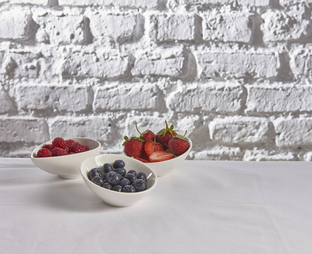 Erdbeeren, Himbeeren, Blaubeeren hinter Ziegelwand weißer Hintergrund - Foto, Bild