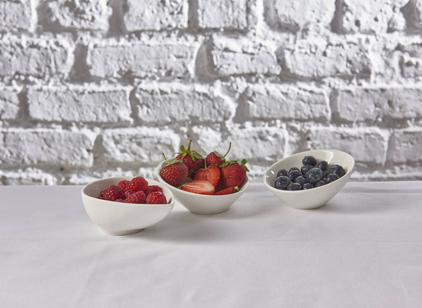 Erdbeeren, Himbeeren, Blaubeeren hinter Ziegelwand weißer Hintergrund - Foto, Bild