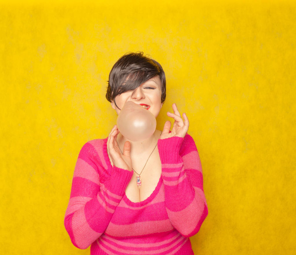 linda mujer con el pelo corto mastica goma de mascar y soplos burbujas sobre fondo amarillo
 - Foto, Imagen
