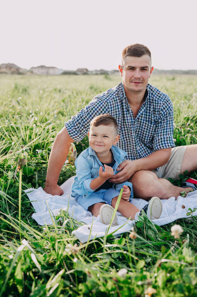Smiling father and baby sitting on meadow in summer day - Fotoğraf, Görsel