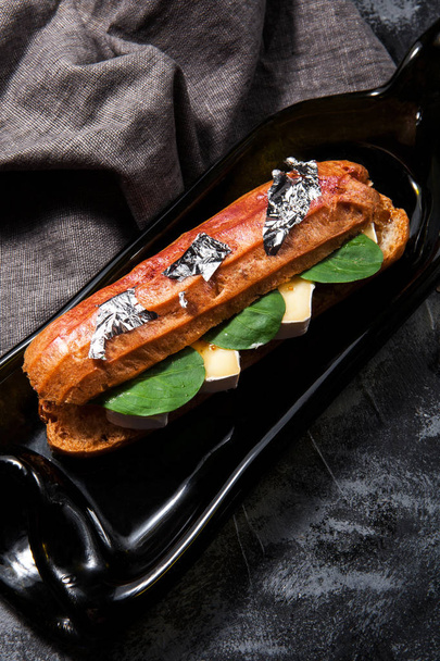 Delicious salty eclair with cheese bree and spinach on a dark stylish background - Photo, Image