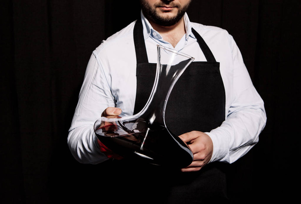 Sommelier is holding wine decanter in his hands on a dark background - Foto, Imagem