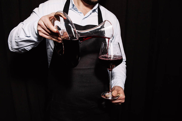 Сомелье наливает красное вино в бокал на темном фоне
 - Фото, изображение