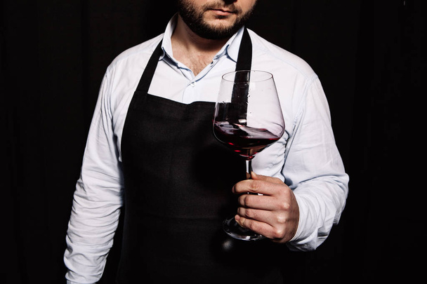 Sommelier is wijnglas met rode wijn in zijn hand op een donkere achtergrond schudden - Foto, afbeelding