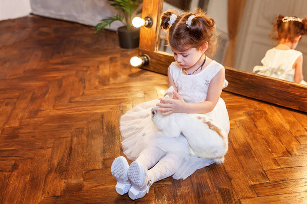 kleines Mädchen sitzt auf dem Boden und spielt mit weißem Hasen in modernem Raum über Spiegel - Foto, Bild