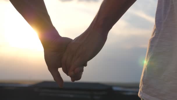 Male hands holding each other at sunset background. Young gay couple standing on roof and joining hands. Concept of male loving and happiness. Rear back view Slow motion Close up - Footage, Video