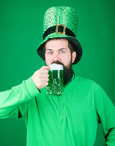 Quenching his thirst. Bearded man toasting to saint patricks day. Hipster in leprechaun hat holding beer mug. Irish man with beard drinking green beer. Celebrating saint patricks day in beer pub - Photo, Image