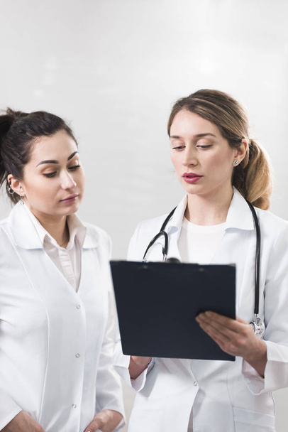 Дві жінки-помічниці, одягнені в білі пальто, розмовляють одна з одною в стоматологічному центрі
 - Фото, зображення