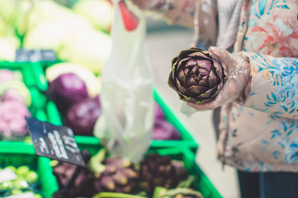 Ψώνια στο σούπερ μάρκετ - γυναικείο χέρι που κρατά ωμή αγκινάρα - για χορτοφάγους, υγιεινή διατροφή και καμία έννοια των τροφίμων ΓΤΟ - Φωτογραφία, εικόνα