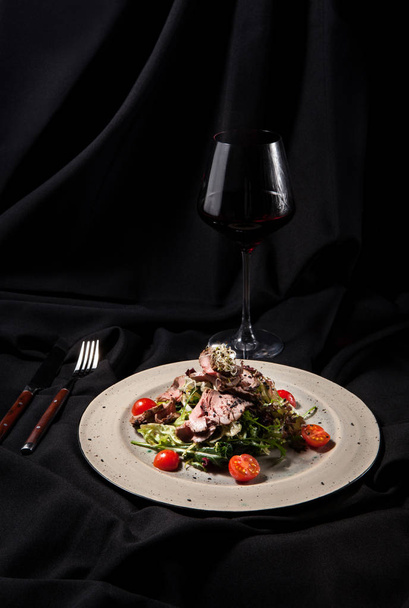М'ясний салат з зеленню, помідори з червоним вином на темному стильному фоні
 - Фото, зображення