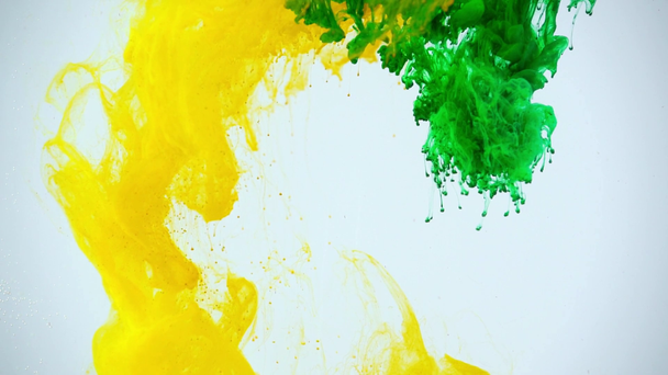 Slow motion opnamen van groene en gele verf oplost in water op grijze achtergrond - Video