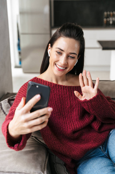 Woman indoors in home on sofa talking by mobile phone. - Photo, Image