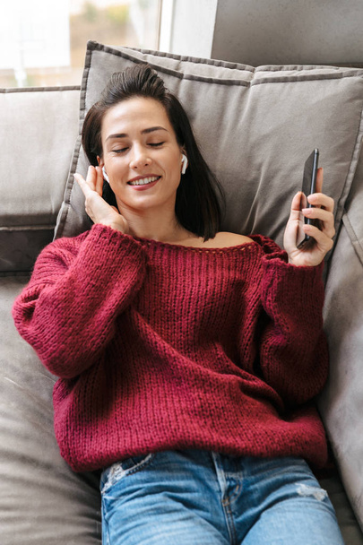 Woman indoors in home on sofa listening music with earphones. - Φωτογραφία, εικόνα