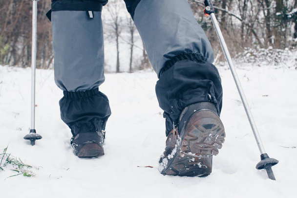 Botas de excursionista con bastones de trekking y polainas que retroceden en el bosque invernal
 - Foto, Imagen